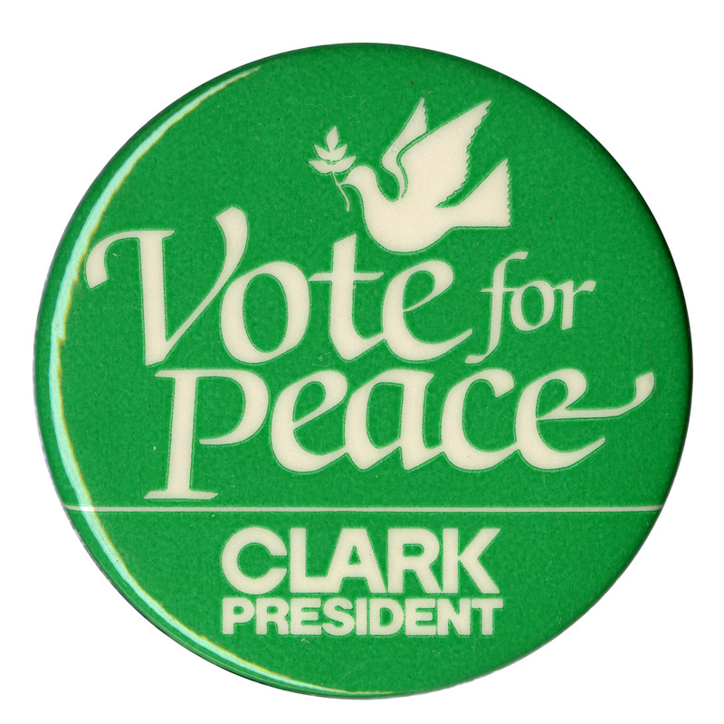 Round, green button with a white drawing of a dove holding an olive branch. White text reads "Vote for Peace CLARK PRESIDENT"