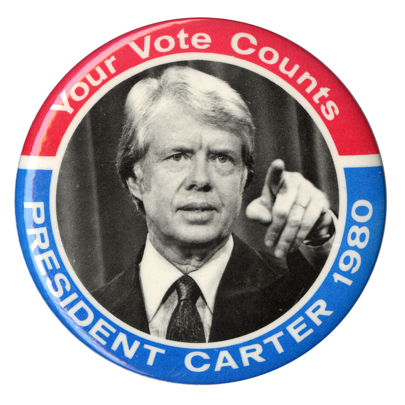 Round button with red and blue border and black and white photograph of Jimmy Carter in the center. White text around the edge reads "Your Vote Counts PRESIDENT CARTER 1980"