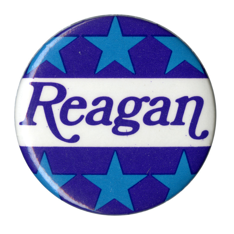 Round button with bands of light blue stars on a dark blue background. Blue text on a white band in the middle reads "Reagan"