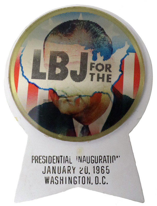 Round button with red, white, and blue flag decorations, the outline of the United States, and a color portrait of Lyndon B. Johnson. Text reads "LBJ for the USA." This is one angle of a holographic button. A white, ribbon-shaped piece of plastic is attached to the button and contains the text "Presidential Inauguration January 20, 1965 Washington, D.C."