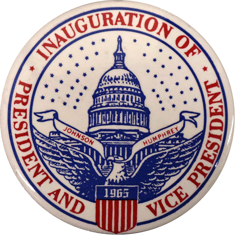 Round, white button with a blue drawing of the US Capitol building and an eagle holding a ribbon that reads "Johnson Humphrey." Around the perimeter of the button is red text reading "Inauguration of President and Vice President." In the bottom center of the button is a red and blue shield with the text "1965." 