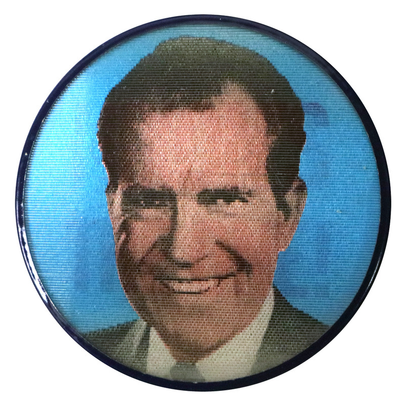 Round, blue button edged in black with a color portrait of Richard Nixon. This is one angle of a holographic button.