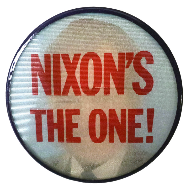 Round, white button edged in black with red text reading "NIXON'S THE ONE!" This is one angle of a holographic button.