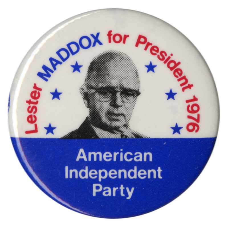 Round, white and blue button with a black and white portrait of Lester Maddox surrounded by six blue stars. Red, blue, and white text reads "Lester MADDOX for President 1976 American Independent Party"