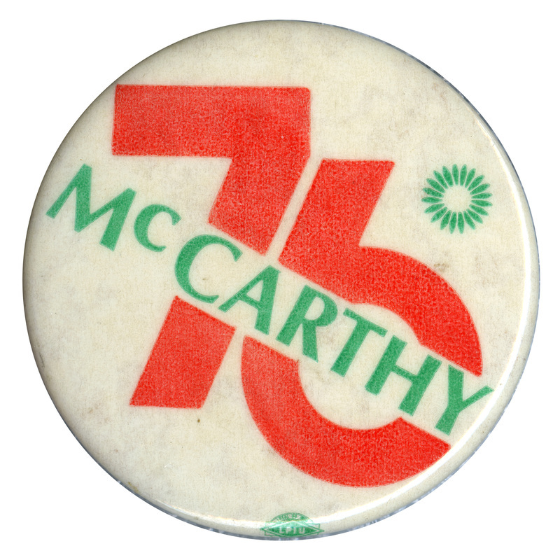 Round, off white button with a green starburst shape and orange and green text reading "McCARTHY 76"