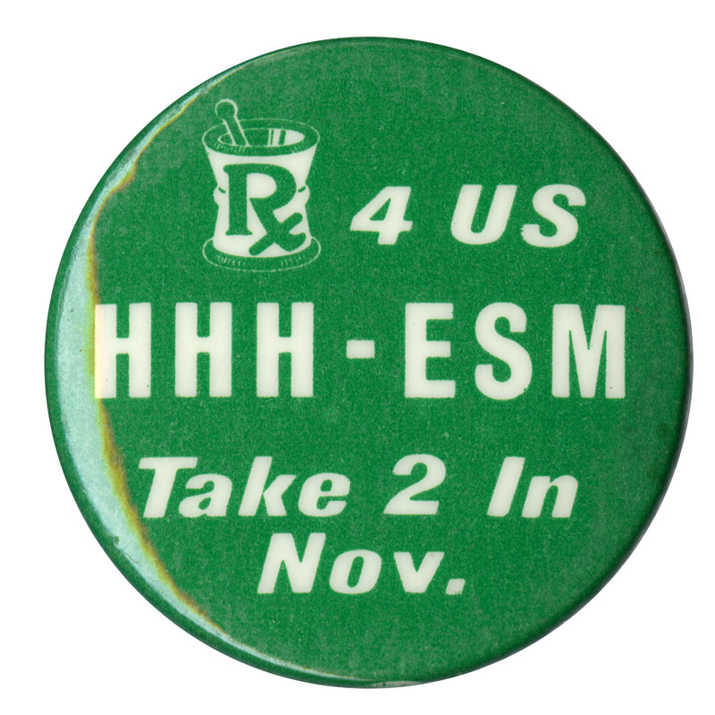 Round, green button with a drawing of a mortar and pestle in white. Green and white text reads "Rx 4 US HHH-ESM Take 2 In Nov."