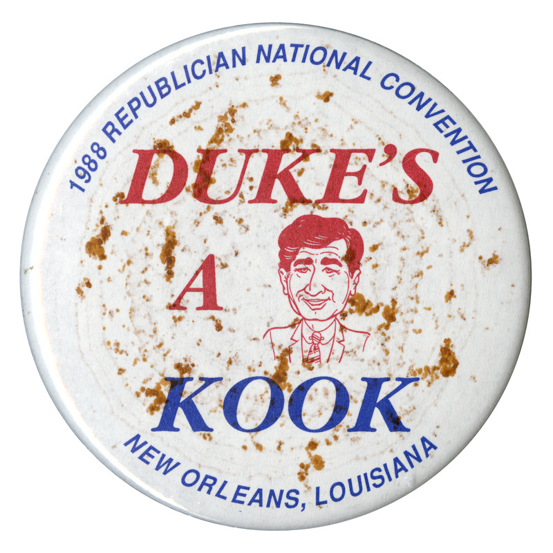 Round, white button with a red caricature drawing of Michael Dukakis. Blue and red text reads "DUKE'S A KOOK 1988 REPUBLICAN NATIONAL CONVENTION NEW ORLEANS, LOUISIANA"