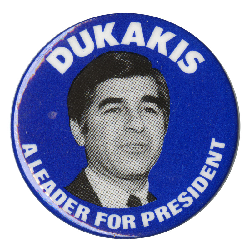 Round, white button with a black and white photograph of Michael Dukakis and white text reading "DUKAKIS A LEADER FOR PRESIDENT"