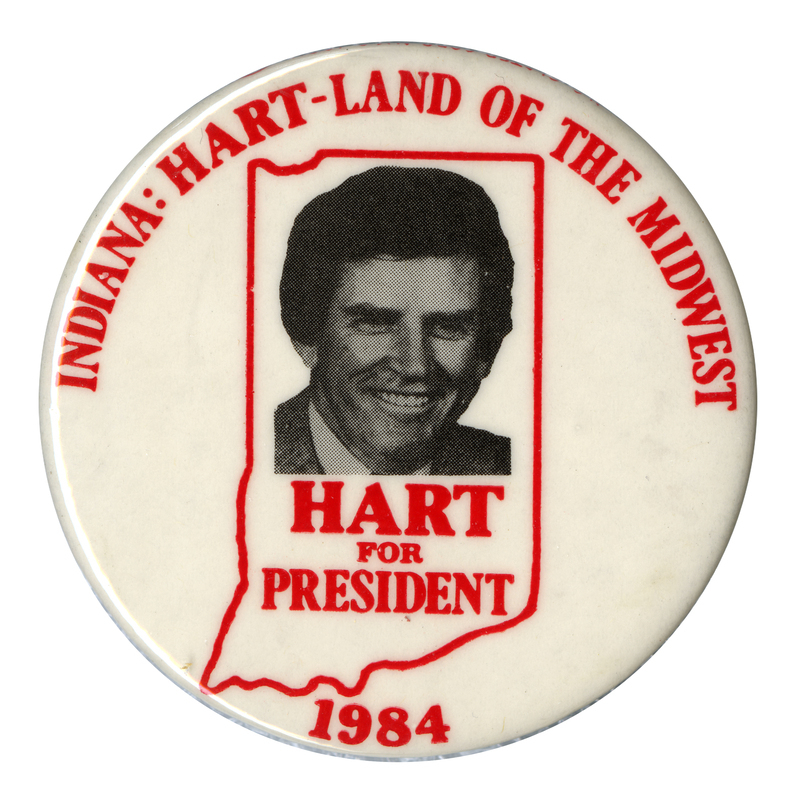 Round, white button with a red outline of the state of Indiana containing a black and white photograph of Gary Hart. Red text reads "INDIANA: HART-LAND OF THE MIDWEST. HART FOR PRESIDENT 1984"