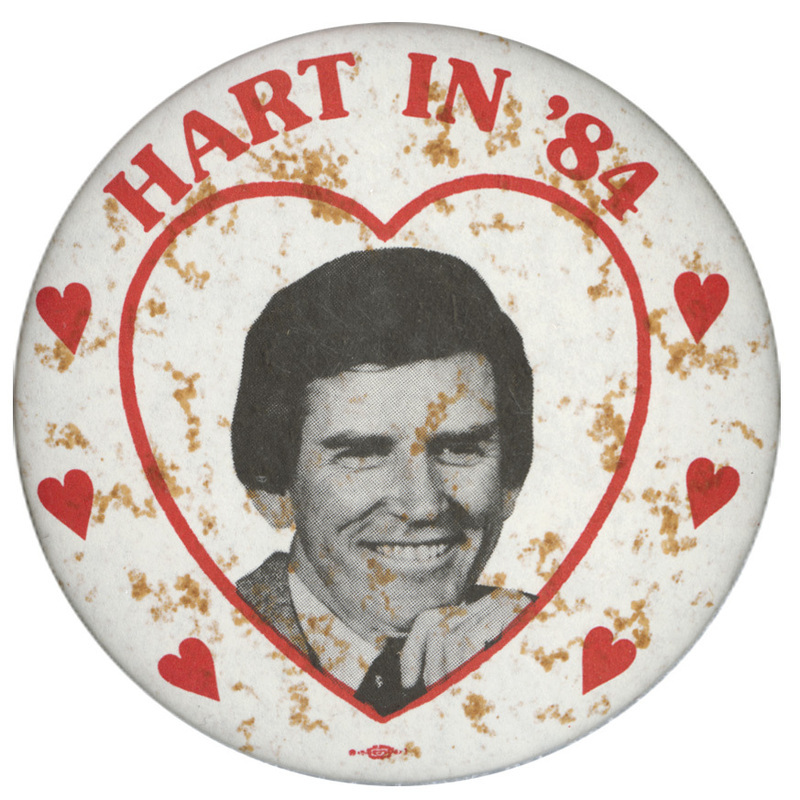 Round, white button with a black and white photograph of Gary Hart and red heart decorations. Red text reads "HART IN '84"
