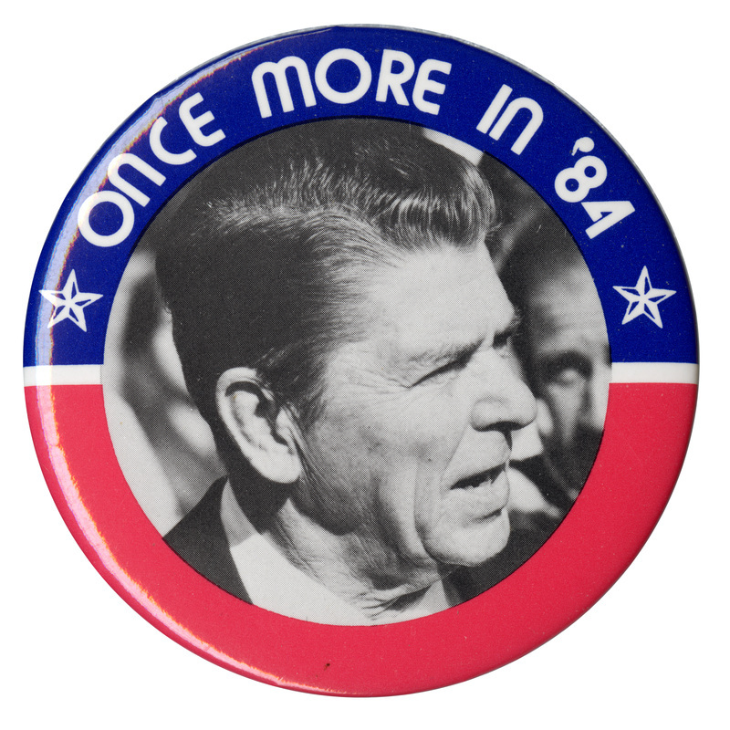 Round button with a blue and red border and a black and white photograph of Ronald Reagan. White text reads "ONCE MORE IN '84"