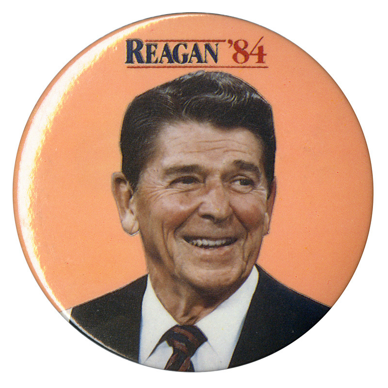 Round, orange button with a color photograph of Ronald Reagan. Blue and red text reads "REAGAN '84"