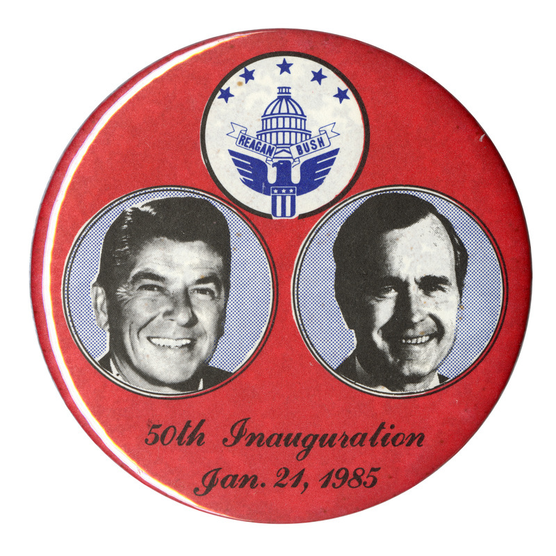 Round, red button with blue and white circles containing black and white photographs of Ronald Reagan and George H. W. Bush and a drawing of the US Capitol surrounded by an eagle bearing a shield, stars, and a ribbon with "REAGAN BUSH" on it. Black text below the photographs reads "50th Inauguration Jan. 21, 1985"