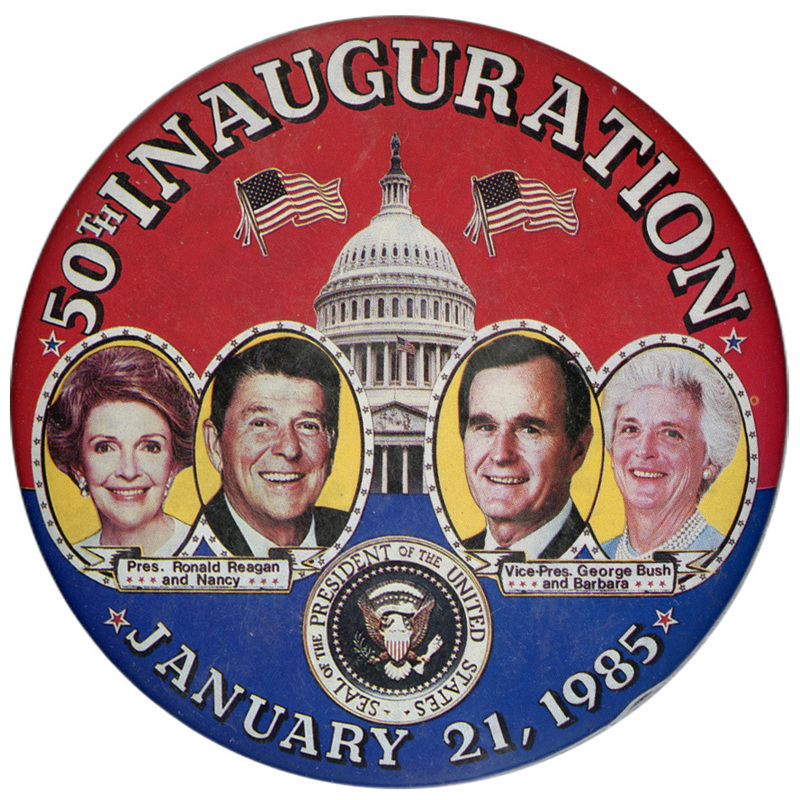 Round, red and blue button with color photographs of Nancy Reagan, Ronald Reagan, George H. W. Bush, and Barbara Bush, against a color photograph of the US Capitol. White text reads "50th INAUGURATION JANUARY 21, 1985"