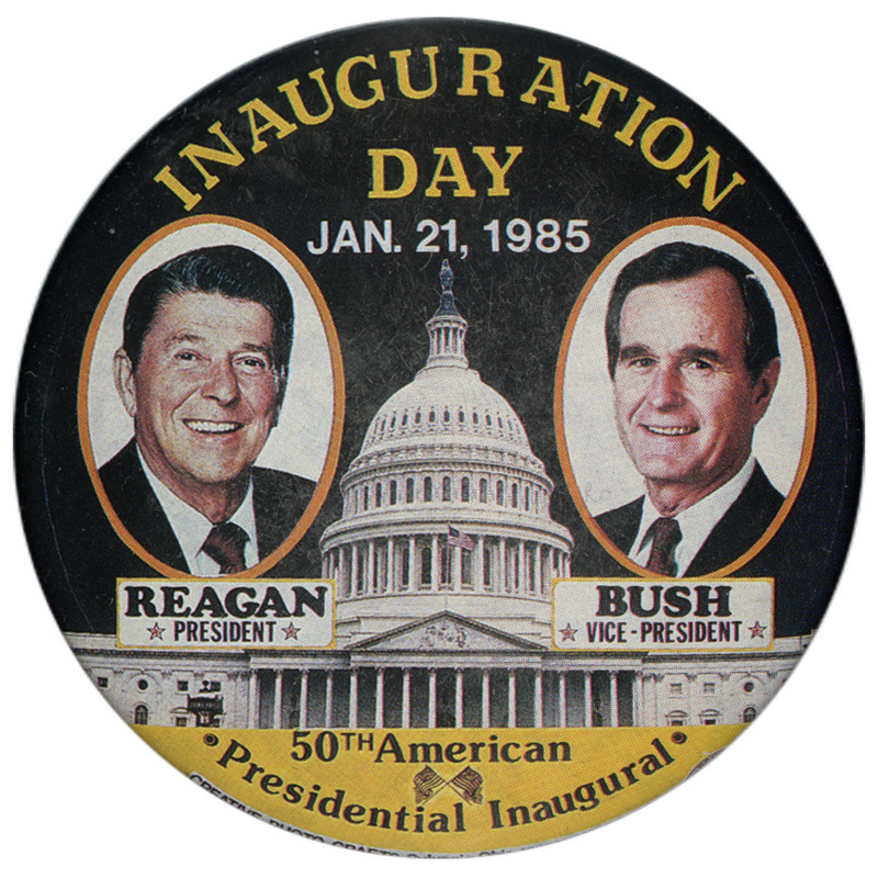 Round, black button with color photographs of Ronald Reagan and George H. W. Bush against a photograph of the US Capitol. Yellow and white text reads "INAUGURATION DAY JAN. 21, 1985 50TH American Presidential Inauguration"