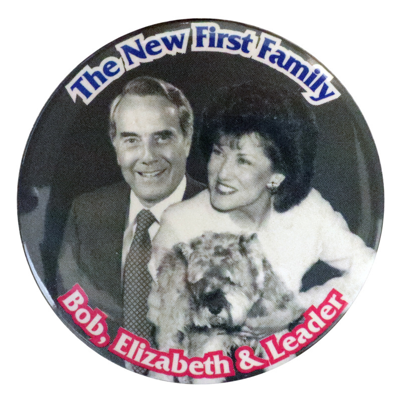Round, gray button with black and white photographs of Bob Dole, Elizabeth Dole, and their dog Leader. Blue and red text reads "The New First Family Bob, Elizabeth & Leader"