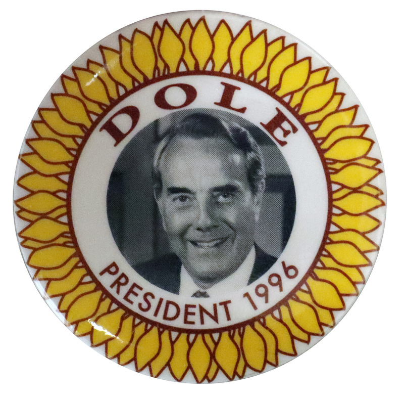 Round, white button with an illustration of a yellow sunflower, the center of which is a black and white photograph of Bob Dole. Brown text reads "DOLE PRESIDENT 1996" 