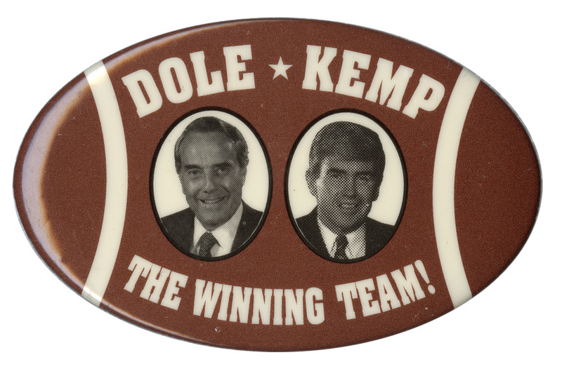 Oval button decorated in brown and white to look like an American football. In the center are black and white photographs of Bob Dole and Jack Kemp. White text reads "DOLE KEMP THE WINNING TEAM!"