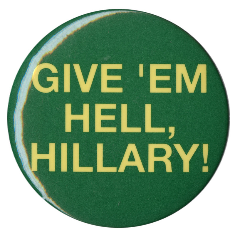 Round, green button with yellow text reading "GIVE 'EM HELL, HILLARY!"