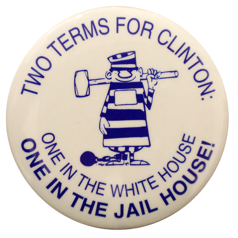 Round, white button with a blue cartoon illustration of a person wearing a striped prisoner's outfit, holding a sledgehammer, a ball and chain attached to one leg. Blue text reads "TWO TERMS FOR CLINTON: ONE IN THE WHITE HOUSE ONE IN THE JAIL HOUSE!"