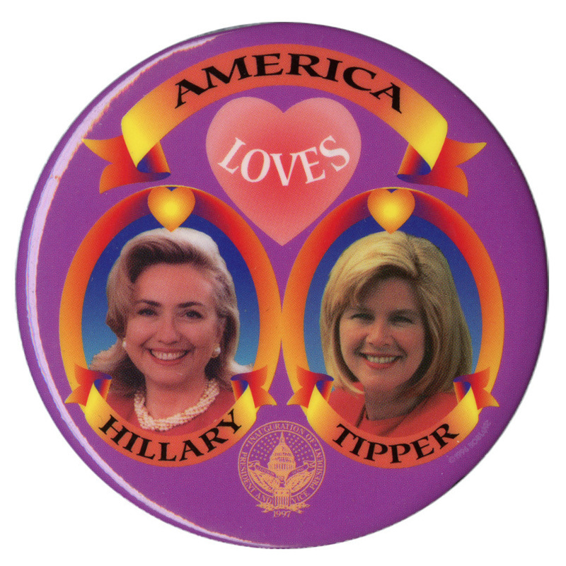 Round, purple button with color photographs of Hillary Clinton and Tipper Gore inside red and yellow frames below a pink heart. Black text reads "AMERICA LOVES HILLARY TIPPER"