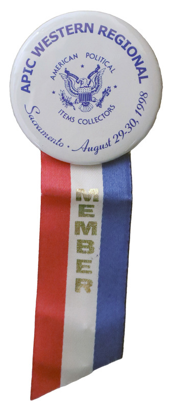 Round, white button with a blue illustration of an eagle holding arrows, an olive branch, and a ribbon. Blue text reads "APIC WESTERN REGIONAL AMERICAN POLITICAL ITEMS COLLECTORS Sacramento August 29-30, 1998." Attached to the bottom of the button is a red, white, and blue ribbon with gold text reading "MEMBER"
