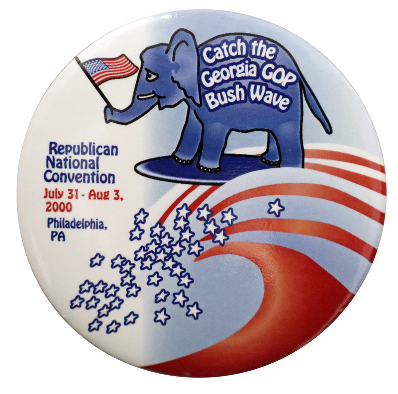 Round, blue and white button with an illustration of a blue elephant holding a US flag with its trunk riding a blue surfboard on a wave composed of red and white stripes and blue and white stars. On the elephant's side, white text reads "Catch the Georgia GOP Bush Wave". Blue and red text on the button reads "Republican National Convention July 31-Aug 3, 2000 Philadelphia, PA"