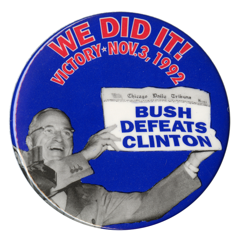 Round, blue button with a black and white photograph of Harry Truman holding up a newspaper in which the original "DEWEY DEFEATS TRUMAN" text of 1948 has been replaced with "BUSH DEFEATS CLINTON." Red text on the button reads "WE DID IT! VICTORY NOV. 3, 1992"