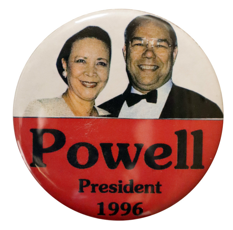 Round, red and white button with a color photograph of Alma and Colin Powell. Black text in the red portion reads "Powell President 1996"