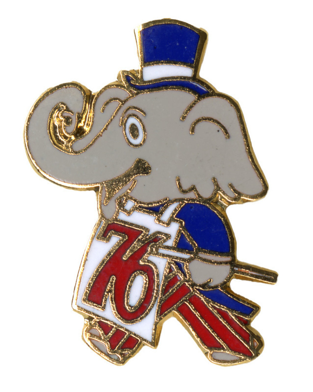Enameled pin in the shape of an elephant wearing a suit, top hat, and white bib with red text reading "76"