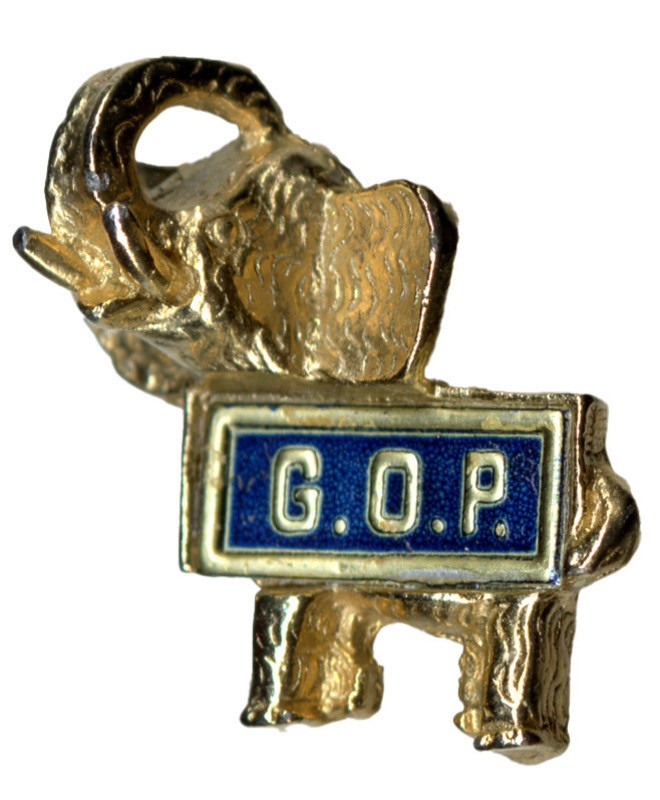 Silver-colored metal pin in the shape of an elephant. In the middle is a rectangular blue badge with silver text reading "G.O.P."