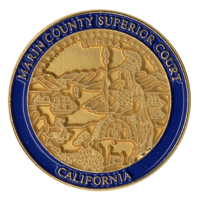 Round pin with an enameled blue border and an embossed illustration of the Marin County Superior Court seal: a woman in historical fighting gear, a bear, and a miner against a background of ships sailing in an inlet. Gold text reads "MARIN COUNTY SUPERIOR COURT CALIFORNIA"
