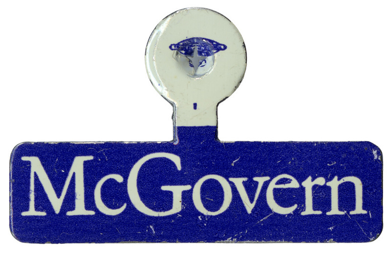 Blue, fold over lapel pin with white text reading "McGovern"