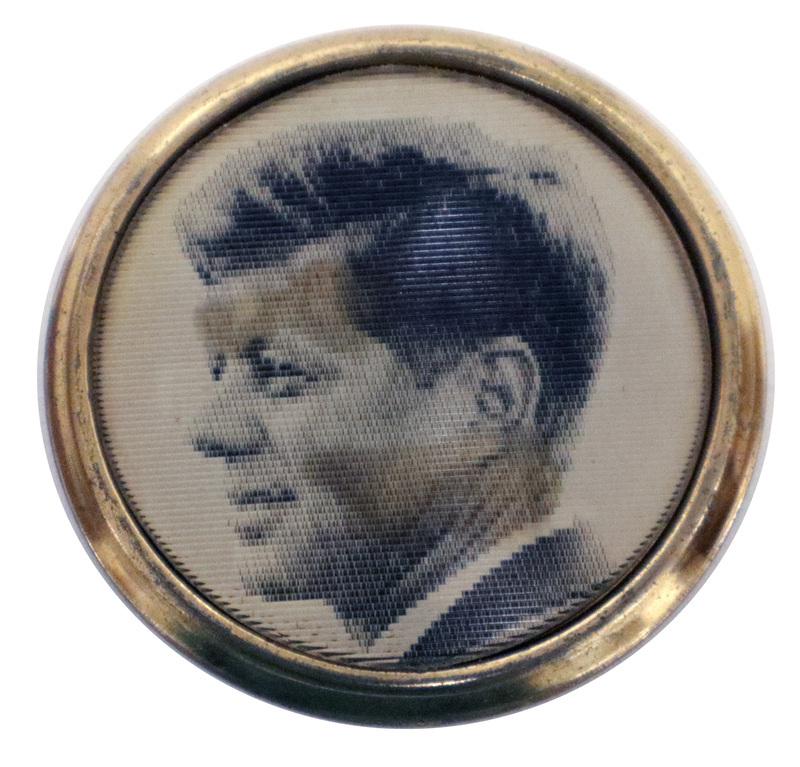 Round button with a gold rim and a black and white photograph of John F. Kennedy. This is one angle of a holographic button.
