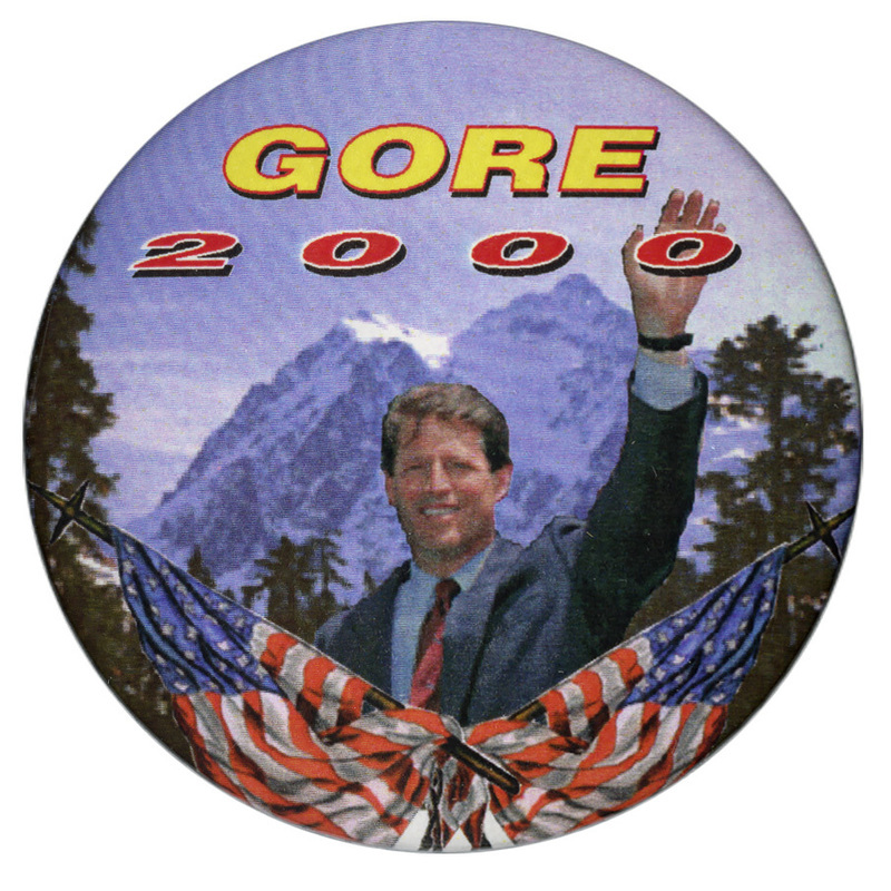 Round button with a color photograph of Al Gore above a color illustration of US flags against a background of trees and snow-covered mountains. Yellow and red text reads "GORE 2000"