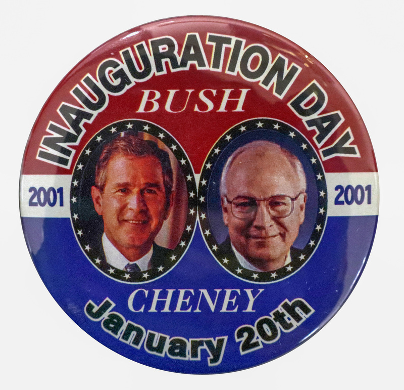 Round, red and blue button with color photographs of George W. Bush and Dick Cheney in the center. Black and white text reads "INAUGURATION DAY BUSH CHENEY 2001 2001 January 20th"