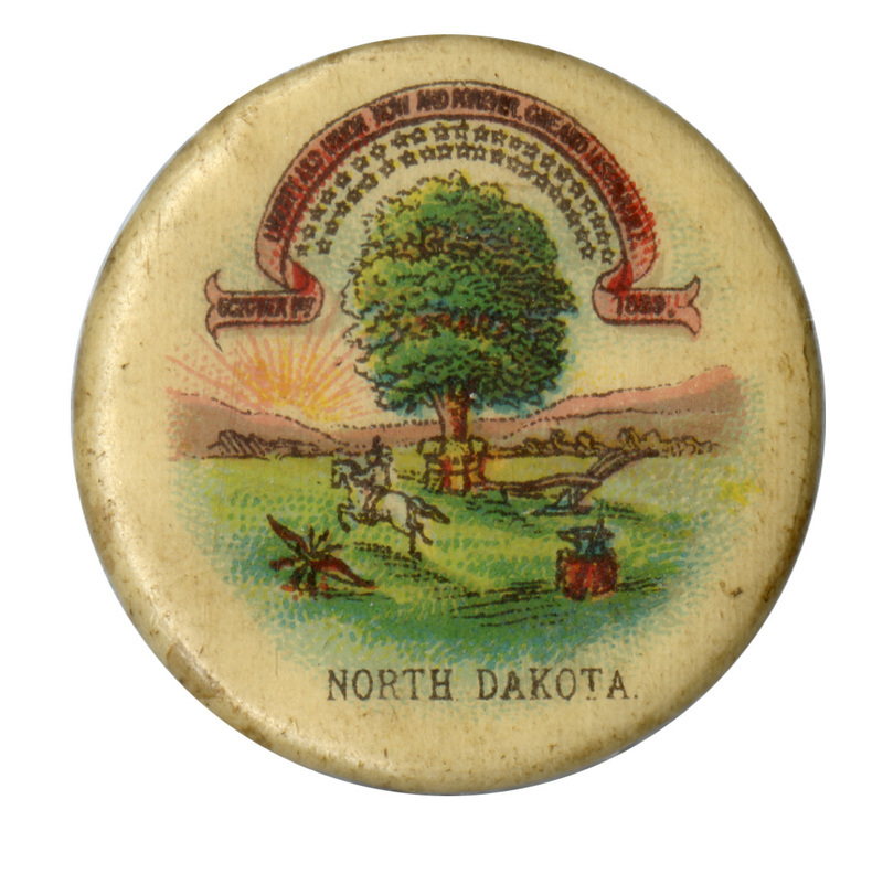 Round, off white button with the state seal of North Dakota, a color drawing of a green tree, a person riding a white horse, and a plow, all under a red banner reading "LIBERTY AND UNION FOREVER, ONE AND INSEPARABLE, OCTOBER 1ST 1899". Black text under the seal design reads "NORTH DAKOTA".