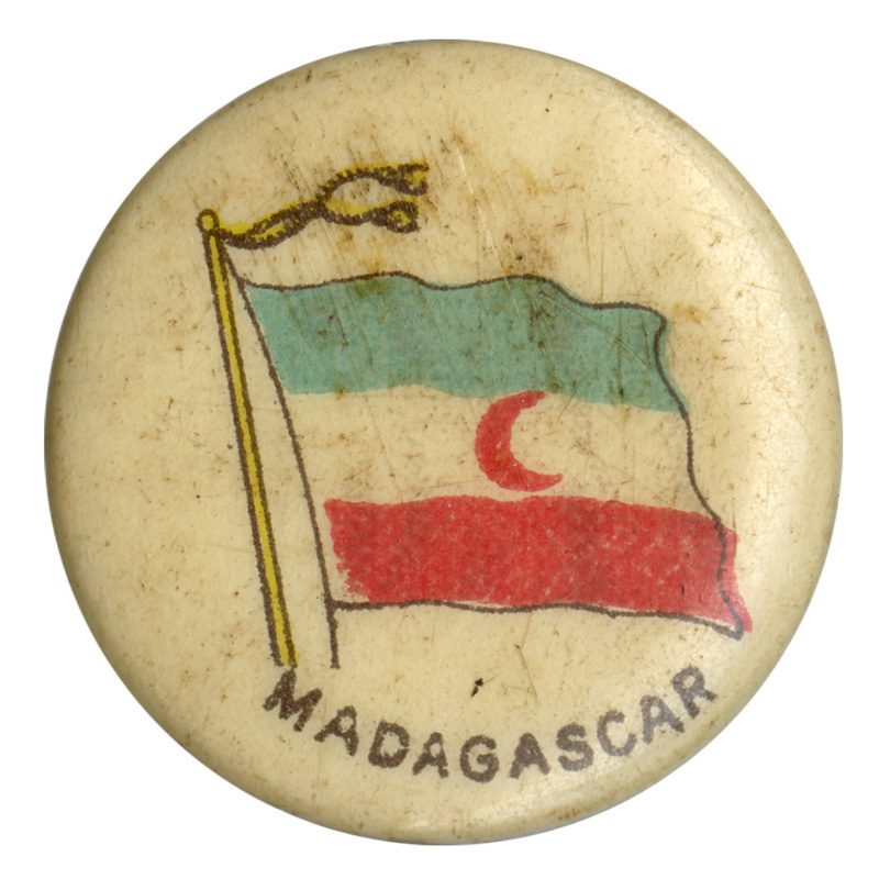 Round, white button with a color illustration of the Malagasy Protectorate (Madagascar) flag, horizontal bands of blue, white, and red with a red crescent in the middle. Black text at the bottom reads "MADAGASCAR."