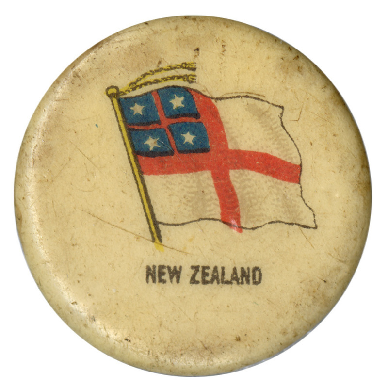 Round, white button with a color illustration of the Flag of the United Tribes of New Zealand, a white field quartered by a red cross, with another red cross in the upper quarter on a field of blue with four white stars in each quadrant. Black text at the bottom reads "NEW ZEALAND"