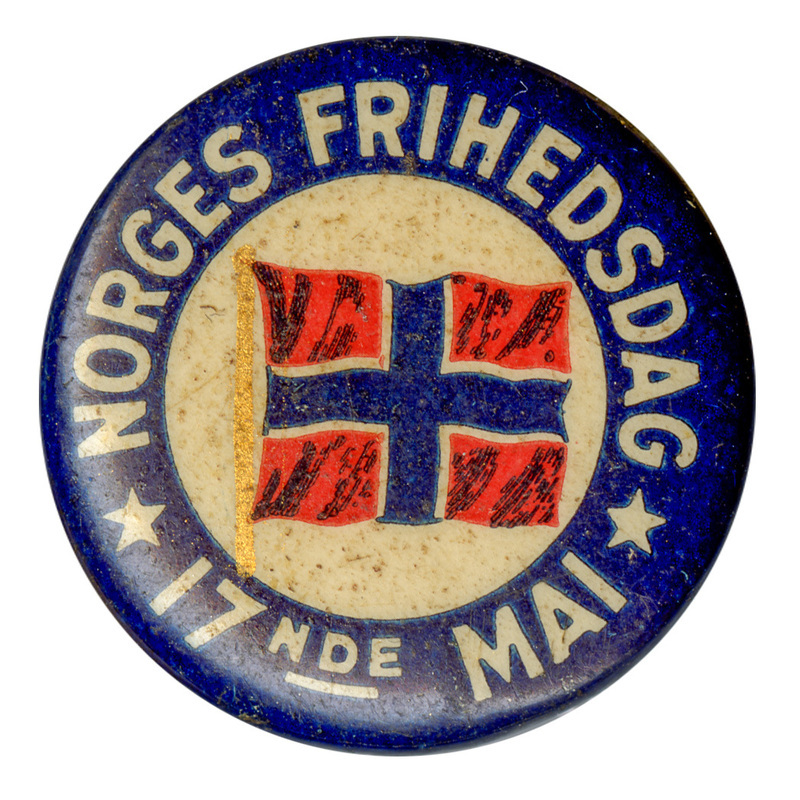 Round button with a blue border. In the center is a color illustration of the flag of Norway, a red field quartered by a blue and white cross. White text around the edge reads "NORGES FRIHEDSDAG 17 NDE MAI" (Norwegian Independence Day, 17th May"