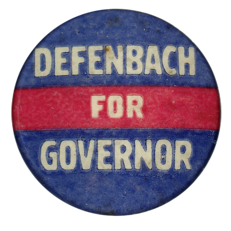Round, blue button with a horizontal red band across the middle. White text reads "DEFENBACH FOR GOVERNOR"