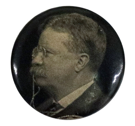 Round, black button with a side-profile, black and white portrait of Theodore Roosevelt. 