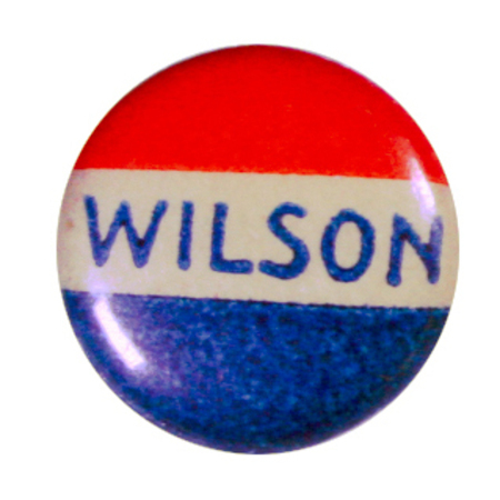 Round button with three red, white, and blue stripes, and blue text reading "Wilson" across the white stripe. 