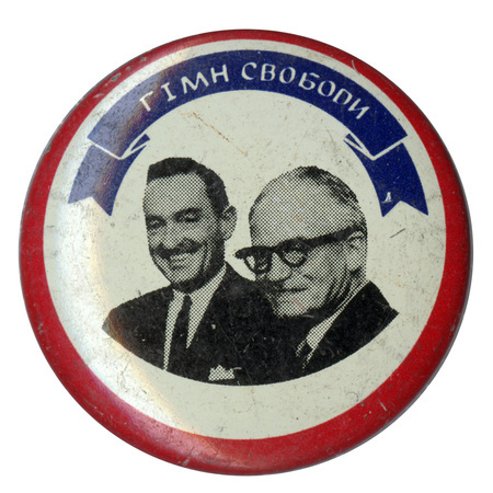 Round, white button with a red outline and a photograph of Barry Goldwater and William Miller. White text in Ukrainian on a blue ribbon translates to "hymn of freedom" or "anthem of freedom."