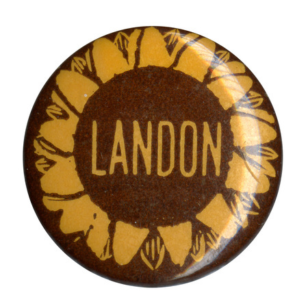 Round, brown button featuring a yellow sunflower with yellow text reading "Landon" in the center.