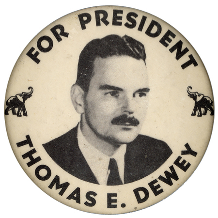 Round, white button with a black and white portrait of Thomas Dewey. Two small elephants are on either side of the portrait. Black text encircles the portrait and reads "For President Thomas E. Dewey". 