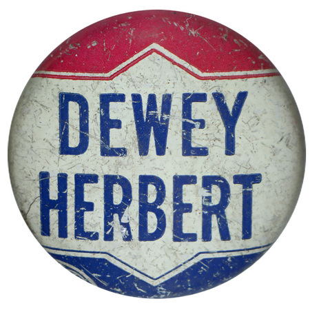 Round, white button with a red and blue decorative element at the top and bottom. Blue text reads "Dewey Herbert" at the center. 