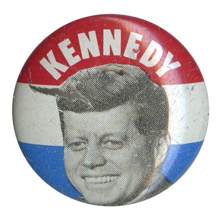 Round button with three horizontal stripes of red, white, and blue. A grayscale portrait of John F. Kennedy at the center. White text reads "Kennedy" at the top.  