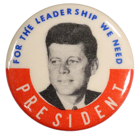 Round, white button with a red border on the bottom half, and a grayscale portrait of John F. Kennedy. Text reads "For the leadership we need President". 