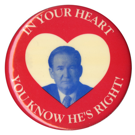 Round, red button with a white heart at the center and a grayscale portrait of Pat Buchanan within it. White text reads "In Your Heart You Know He's Right!" and encircles the portrait. 